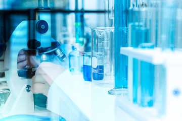 Hand of scientist using microscope and chemical liquid in test tubes with lab glassware, science laboratory research and development concept in blue tone.