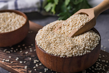 White sesame in a wooden spoon on dark table, Sesame oil in jar and seeds concept.