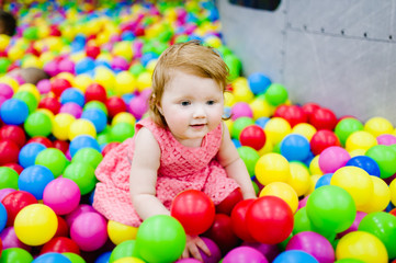 Portrait little cute baby girl princess infant 1-2 year standing and play with balloons, colorful balls in playground, ball pit, dry pool for birthday party. Celebration first year concept.