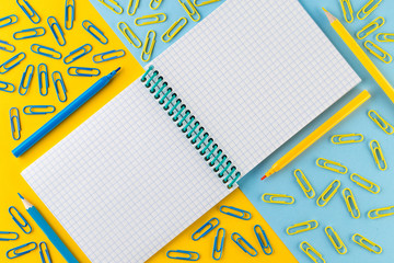 Paper clips and Notepad on bright yellow and blue paper background