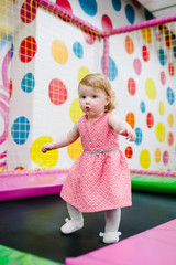 Portrait little cute baby child girl princess infant 1-2 year playing and jumping on a trampoline in children's playroom, indoor on birthday party. Celebration concept holiday, event, entertainment.