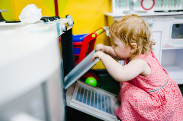 Happy little kid, baby girl one year, playing with a toy kitchen in children room, kindergarten or...