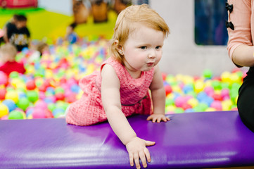 Fototapeta na wymiar Happy laughing girl playing with toys, colorful balls in playground, ball pit in the gaming room. Little cute child having fun in ball pit on birthday party in kids amusement park.