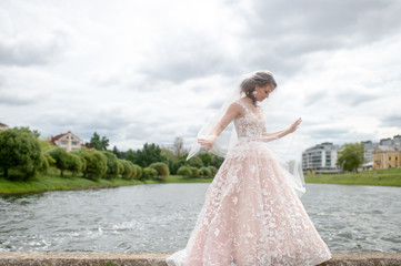 Beautiful  bride in wedding dress with veil over her face posing outdoor with lake on background.