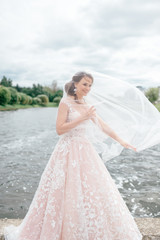 Fototapeta na wymiar Beautiful bride in wedding dress with veil over her face posing outdoor with lake on background.