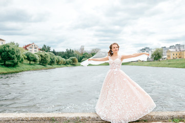 Obraz premium Beautiful bride in wedding dress with veil over her face posing outdoor with lake on background.