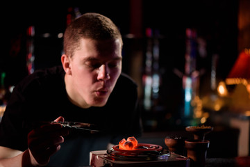 Shisha hookah, red hot coals. Man blows coals for sparks fly.