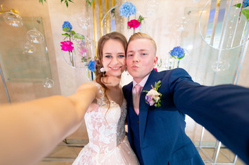 Funny wedding couple taking selfie on decorative wall background