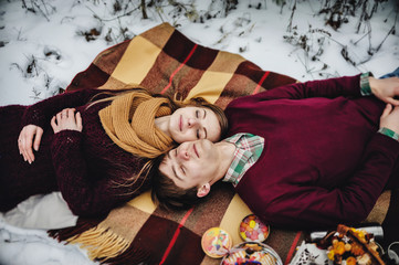 Man and girl is lying on a blanket at the winter picnic on the Valentines Day in a snowy park, forest. Christmas holiday, celebration. Top view, flat lay.