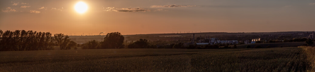 Panorama with setting sun, industrial plants and wind turbines on the horizon