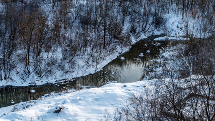 Among the slopes of a deep ravine, covered with bushes and trees, flows a small river. In the dark cold water reflected bushes and trees and the sun.