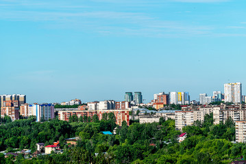 Fototapeta na wymiar In the foreground one-storey buildings and trees. In the background, high-rise buildings. This is the outskirts of Perm. June, early morning, cloudless sky.