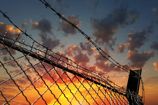 Barbed wire fence against a dramatic sky at sunset. The concept of restriction of freedom of movement.