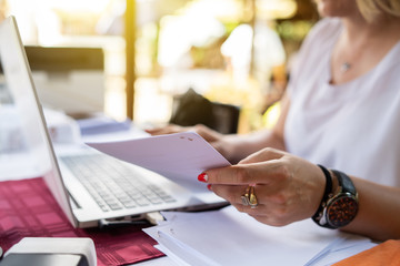 Freelancer woman working on her laptop entering data from document typing while sitting by the table at terrace checking paperwork from the account database invoice loan