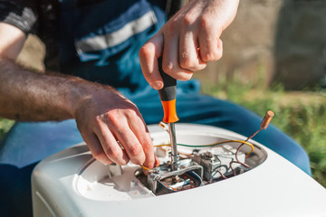 Repair and maintenance of the water heater. A man twists a screwdriver element of the water heater. Outdoor. Close up