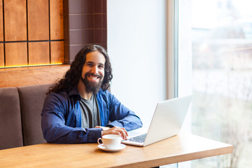Portrait of satisfied handsome intelligence bearded young adult man freelancer in casual style sitting in cafe and working in laptop,looking at camera, bussinessman in office. Indoor,lifestyle concept