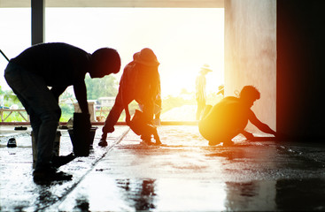 Silhouette group of workers build the cement floor in the house under construction with light of sunset.
