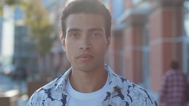Portrait of nice-looking confident young man with mixed race beauty appearance looking straight standing outdoors in the city center under sunlight.