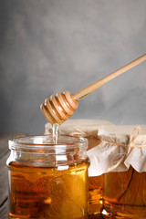 Pouring aromatic honey into jar, closeup. Honey in glass jars and honeycombs wax on wooden background. Wooden stick , instruments