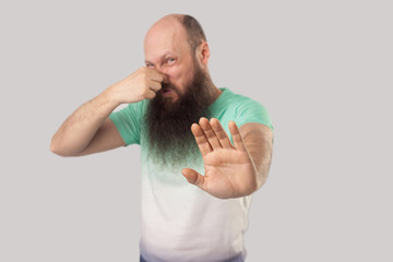 Bad smell, stop. Portrait of confused middle aged bald man with long beard in light green t-shirt...