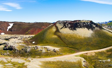 View on surreal volcanic landscape with green black volcano crater and red mountain range against...