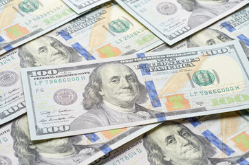 Background from chaotically lying of notes for one hundred dollars. In the foreground, one hundred-dollar bill.