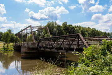 Fototapeta na wymiar Metal Bridge Over River Under Blue Cloudy Skies