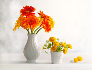 Beautiful bouquet of red and yellow flowers in white vase on wooden table, front view. Autumn still...