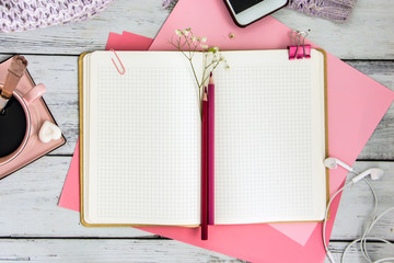 An open notebook in a cage on pink album sheets, next to two red pencils, a pink coffee chicken, an old pocket watch on of the wooden table. A flat lay style composition, a top view 