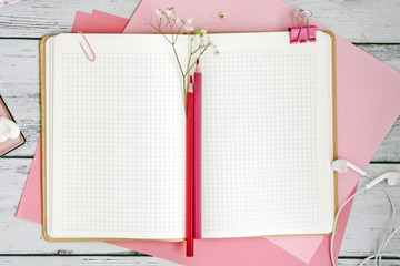 An open notebook in a cage on pink album sheets, next to two red pencils, a pink coffee chicken, an old pocket watch on of the wooden table. A flat lay style composition, a top view 