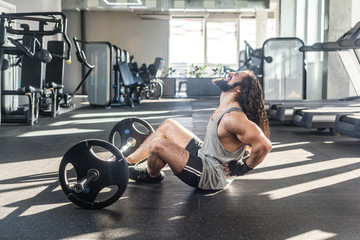 Portrait of injury young adult man athlete with long curly hair working out in gym, sitting on...
