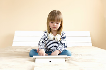 Little blond girl streaming online on tablet with headset.