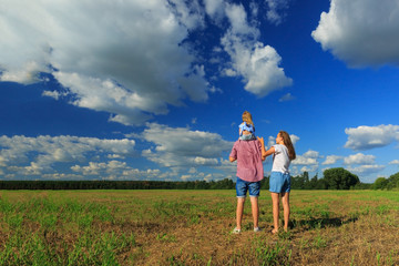 Mom dad and daughter look at the sun in the wheat field. Back view.