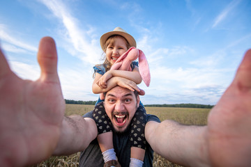 dad keeps his daughter sitting on his shoulders. cheerful father and daughter take selfies at arm's...
