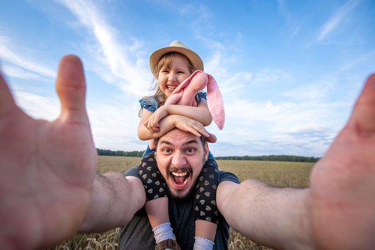 dad keeps his daughter sitting on his shoulders. cheerful father and daughter take selfies at arm's length camera. look through the lens