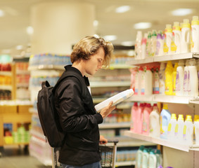 Man shopping in supermarket reading product information.(washing powder,detergent)