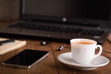  Laptop (notebook) mobile phone (smartphone) and notepad with pen on old wooden table. Work place modern.Cup of coffee