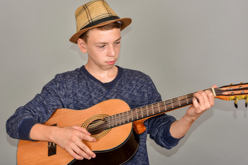 A boy plays the guitar on a gray background in the studio, wide-angle close-up photo.