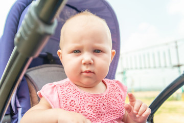 A child in a pushchair outside in the park, a little girl looks into the camera.