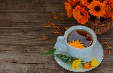 a Cup of tea with a bouquet of calendula in a basket on a wooden background with a copy of space