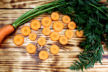 Obraz na płótnie Canvas Fresh crop of carrots with tops and sliced in circles lies on the table