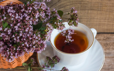 a Cup of hot aromatic tea with oregano herbs in a basket on a wooden background