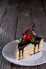 A biscuit cake is filled with chocolate with slices of chocolate tile, cherry and green leaf on wooden background.