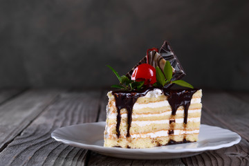 A biscuit cake is filled with chocolate with slices of chocolate tile, cherry and green leaf on wooden background.