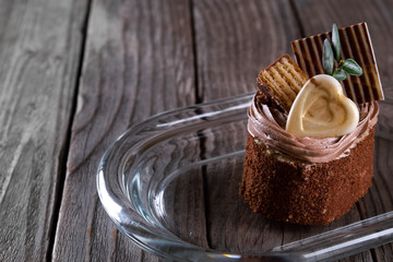  A biscuit cake is sprinkled with cocoa with chocolate cream, a heart of white chocolate, a slice of chocolate tile  and a delicious waffle on wooden background.