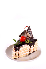 A biscuit cake is filled with chocolate with slices of chocolate tile, cherry and green leaf on wooden background.