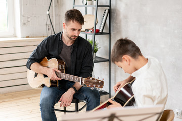 A professional teacher watches the movement of his student's hands while he plays the guitar