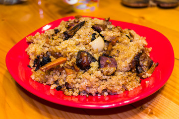 Uzbek pilaf with meat in a red plate on a wooden table, close up