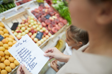 High angle closeup of unrecognizable young woman holding shopping list while buying groceries at...