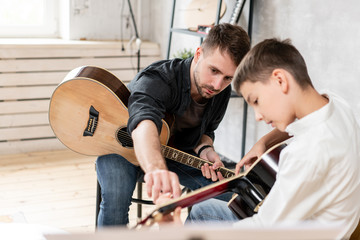 Two brother playing guitar. Older brother teaches younger one to play chords correctly